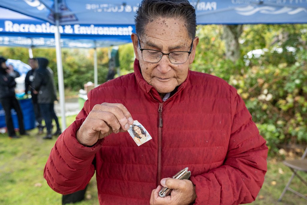 Lisa Marie Young's photo, taken when she was 16, is taken out of a wallet and shown by her grandfather who is wearing a red jacket.