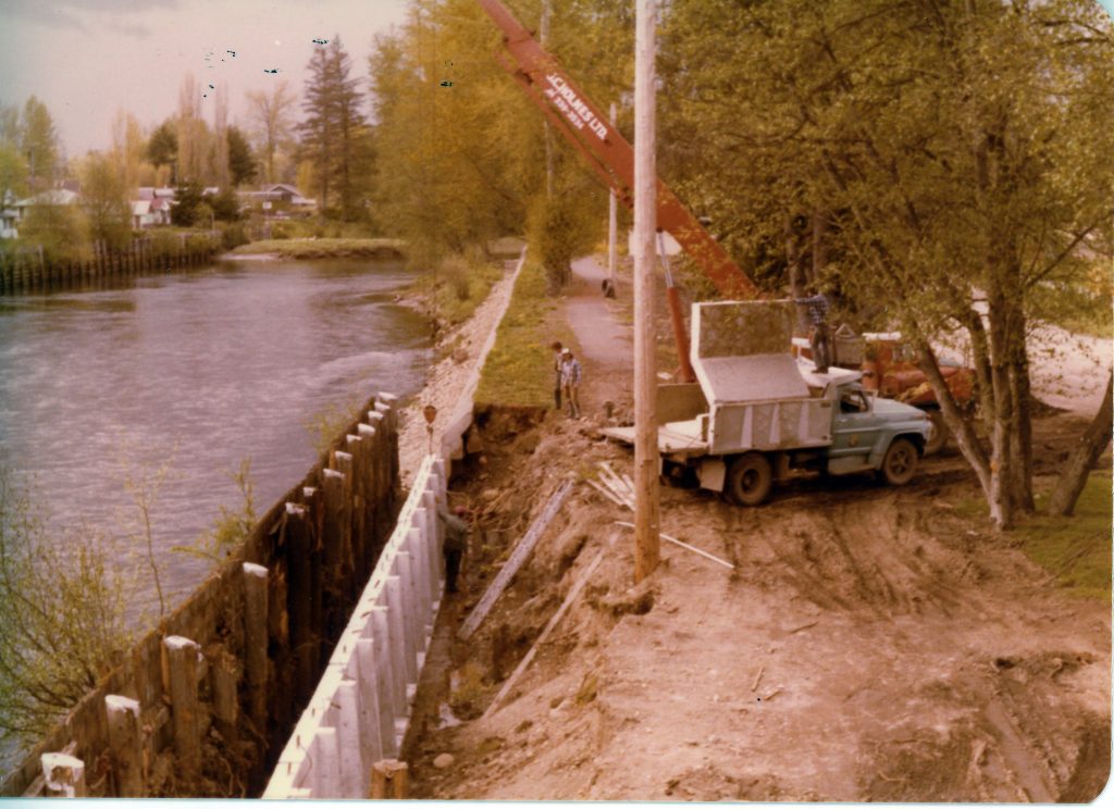 An old photograph that looks to be from about 1970 showing construction along the retaining wall along the river.