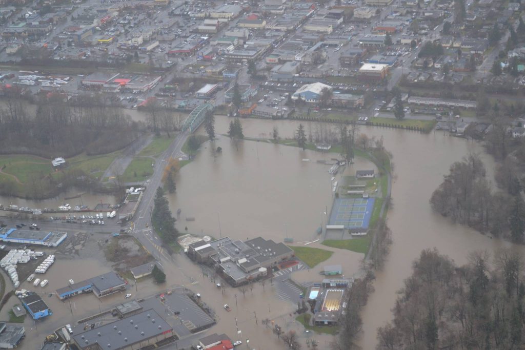 An aerial view of flooding on a dreary day. An entire field is flooded, and the water has flooded most roads around the city.