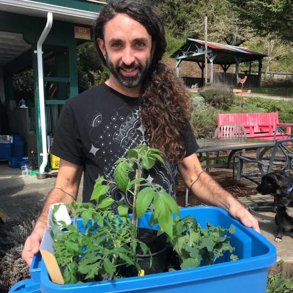 A man holds a bin with potted plant starters in it.