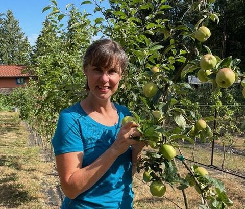 A photo of a woman standing next to an apple tree