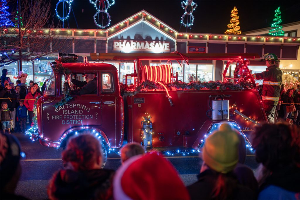 Ladysmith Light Up Parade 2024 showing a photo of a vintage fire truck from Salt Spring Island with Christmas lights on it driving down the Main Street in Ladysmith with a crowd watching
