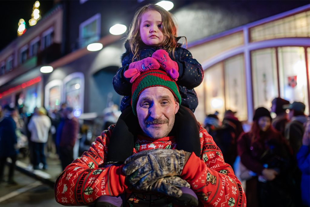 Photo of a man with a moustache, wearing a red Star Wars Christmas sweater with a small girl sitting on his shoulders.