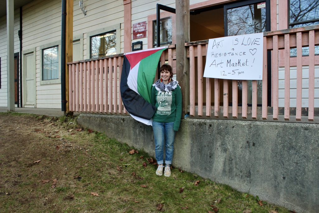 Stephanie Abbat-Slater stands in front of a Palestinian flag outside of the winter art market.