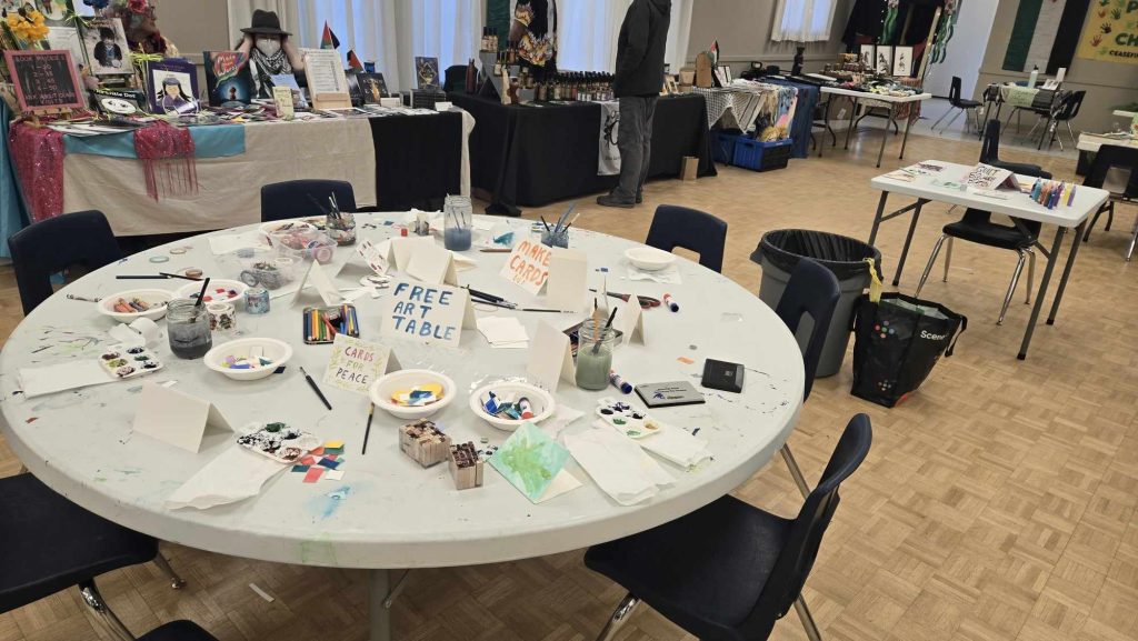 Art is laid out on one of the art tables at Comox Valley for Palestine’s winter market fundraiser event. A sign on the table reads "Free art table"