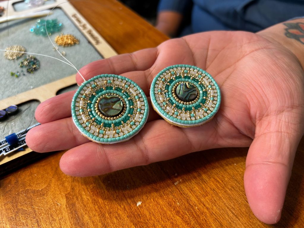 Indigenous maker Larissa Yamelst holds a pair of flat stitched earrings, she will be featured at the market.