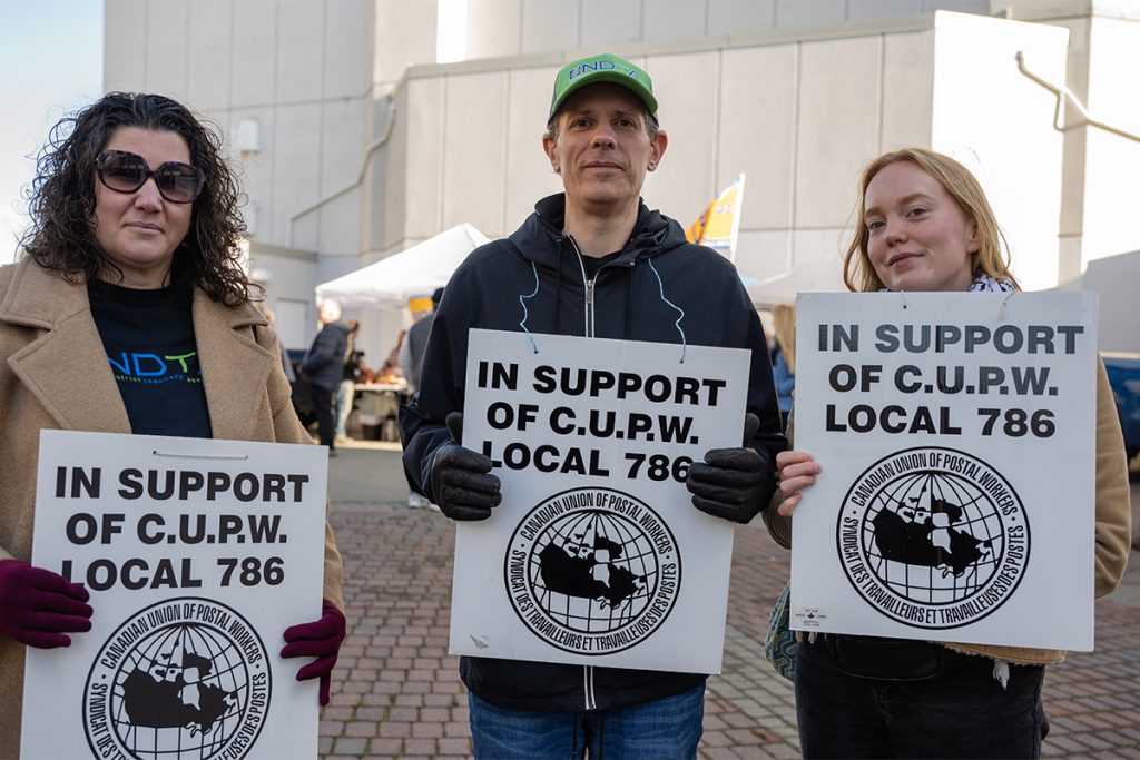 Three teachers hold signs reading In support of CUPW Local 786