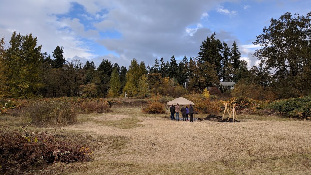 A pop up tent sits at the back of an open field lined with trees