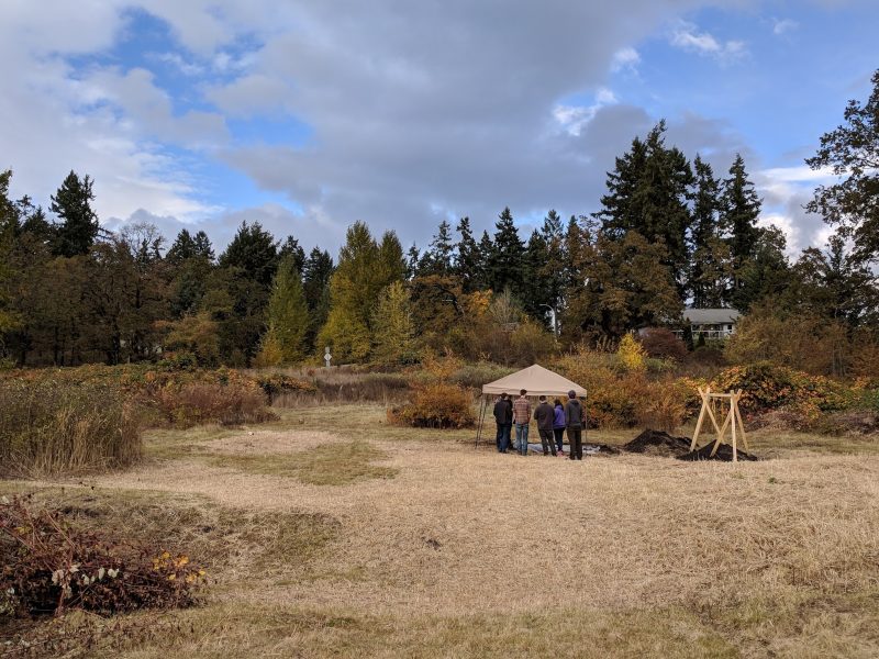A pop up tent sits at the back of an open field lined with trees