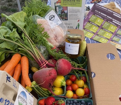A box of food shows some of what can be purchased with the farmers’ market coupons from the Comox Valley Farmers’ Market. There are carrots, tomatoes, beets, honey and chicken