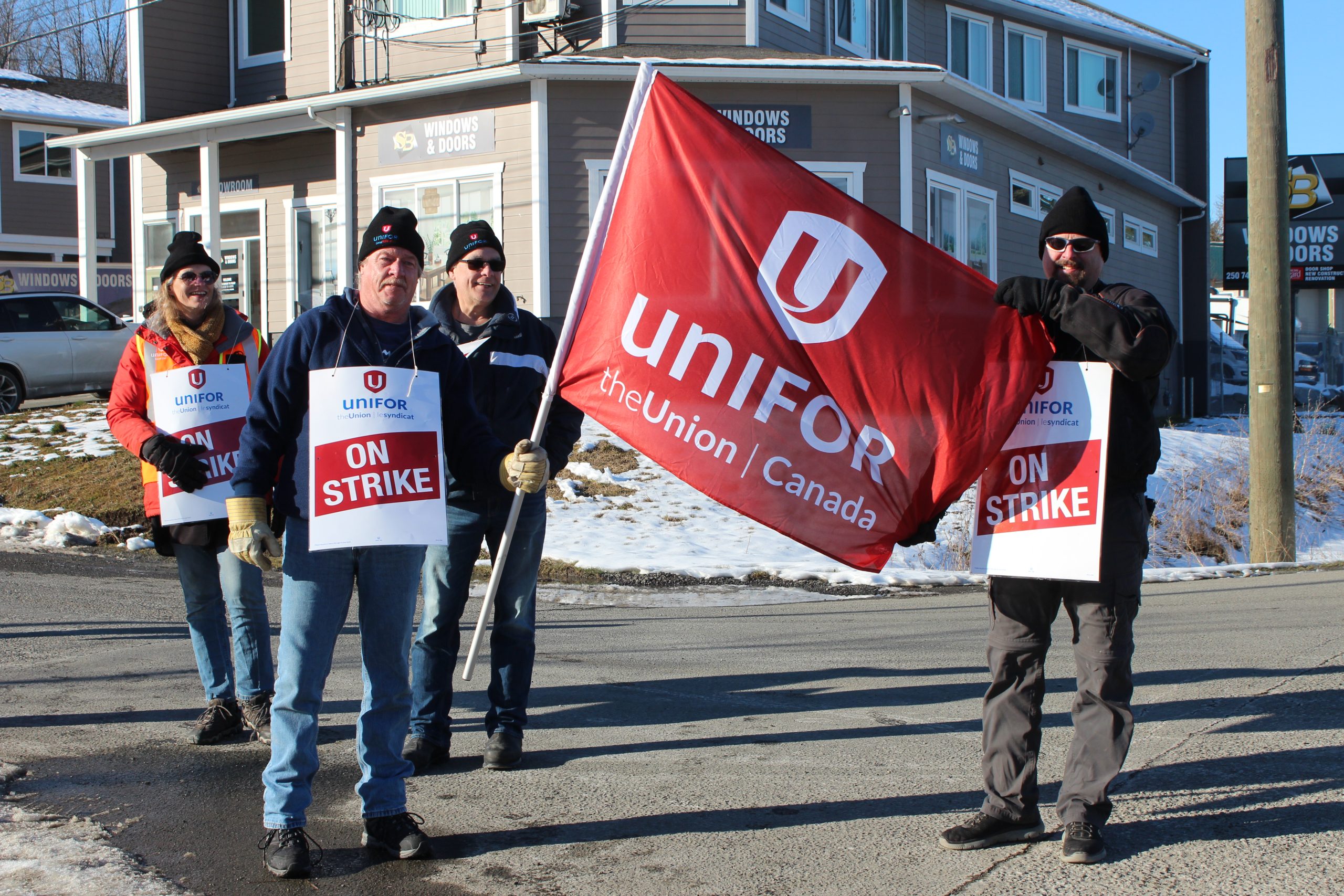 Cowichan transit workers hold up a red Unifor flag and signs.