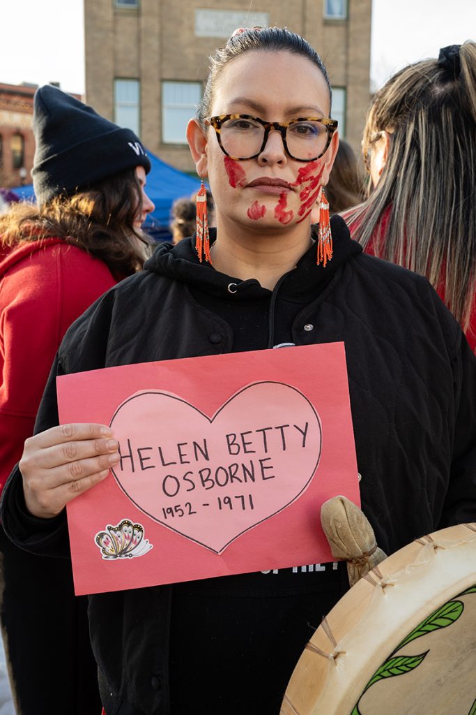 Anna Mckenzie holds a sign in memory of family friend Helen Betty Osborne who was murdered in The Pas, Manitobia in 1971 at the MMIWG2S+ march in Nanaimo on Feb. 14, 2025