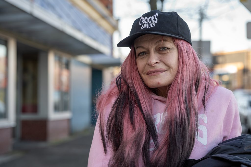 Photo of a woman with pink hair and a pink sweatshirt and black ball cap.