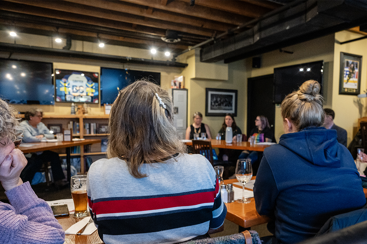 Audience members seated at a table listen to the panel on women's health in the Cowichan Valley. The photo is taken from behind them.