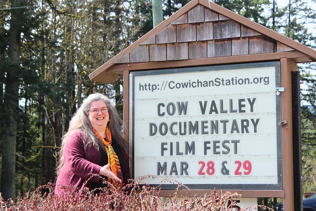 A woman stands in front of a sign that says Cow Valley Documentary Film Fest Mar 28 and 29.
