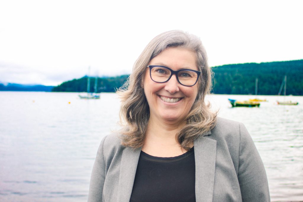 A woman smiling and standing in front of water and sail boats.