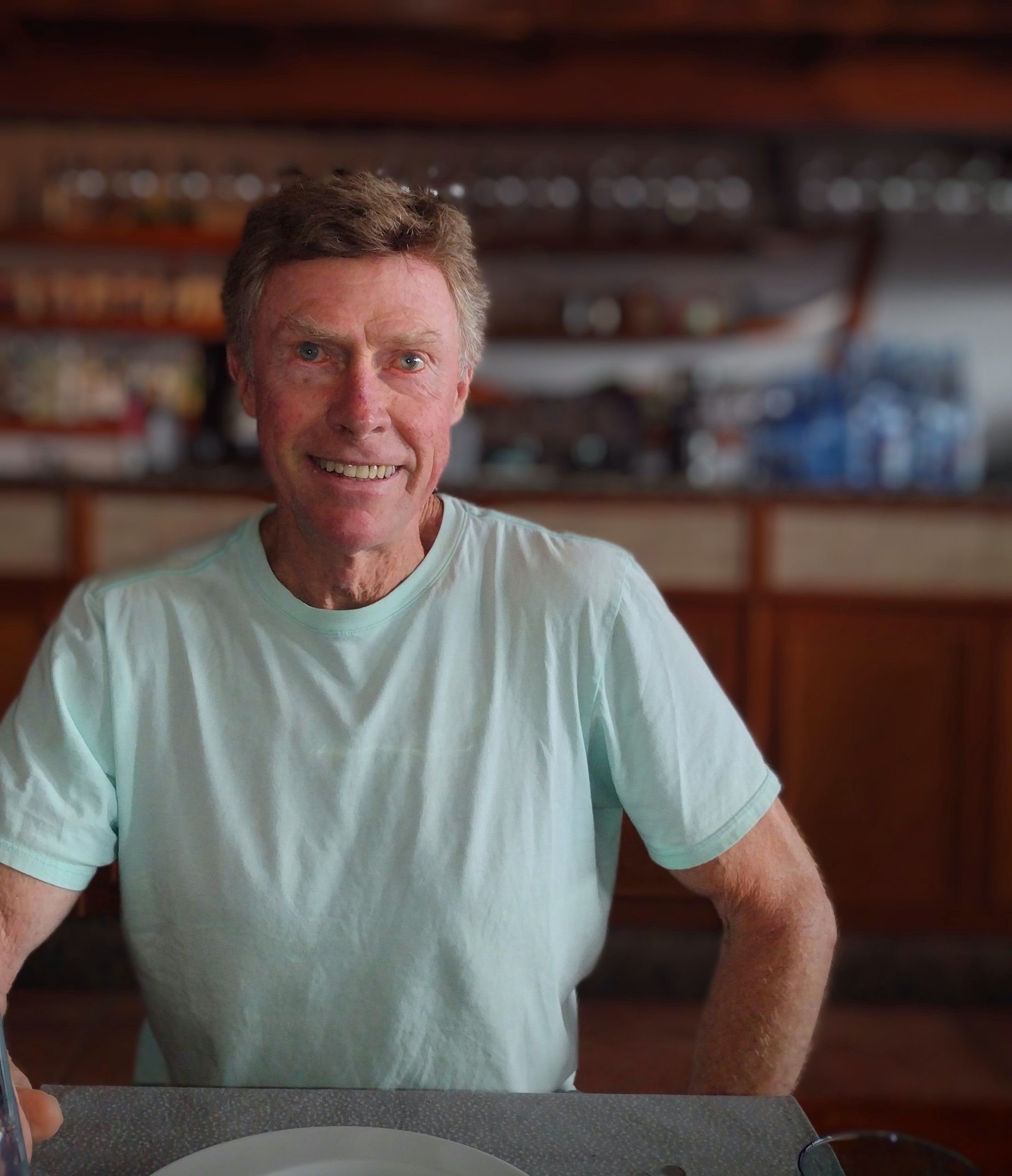 A man in blue shirt sitting looking at the camera at a restaurant.