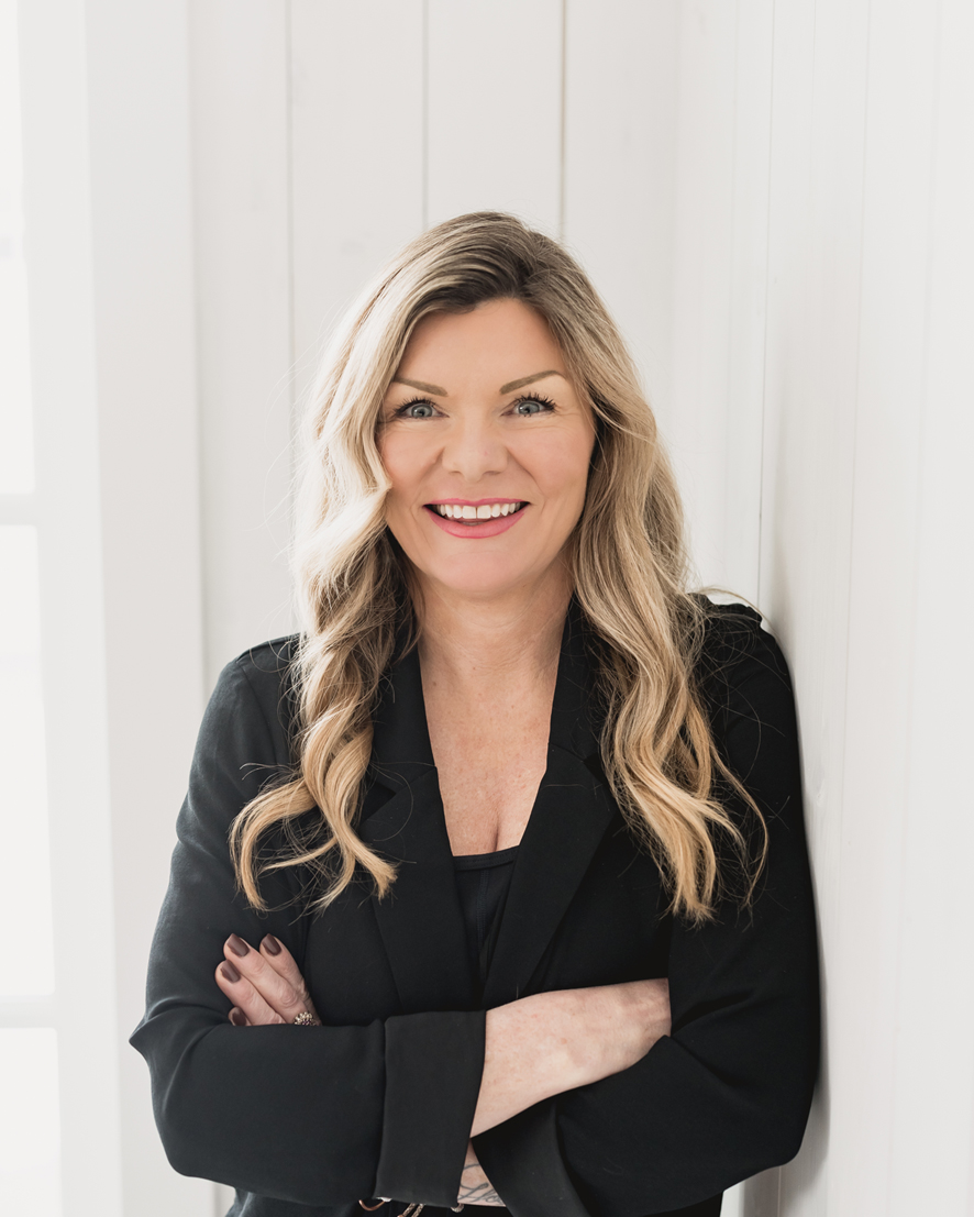 A woman standing in front of a white wall in a black shirt.