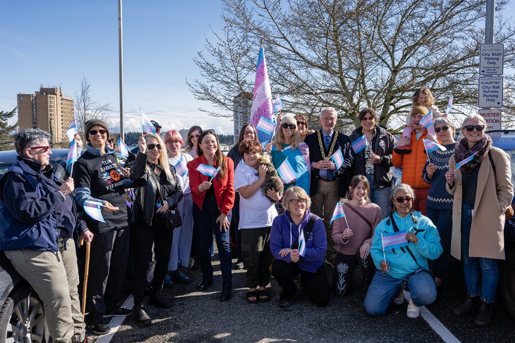 A group of people smiling and waving small trans pride flags