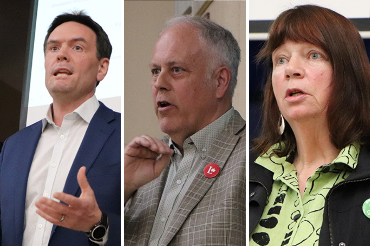 Three people standing and talking at an all-candidates meeting.