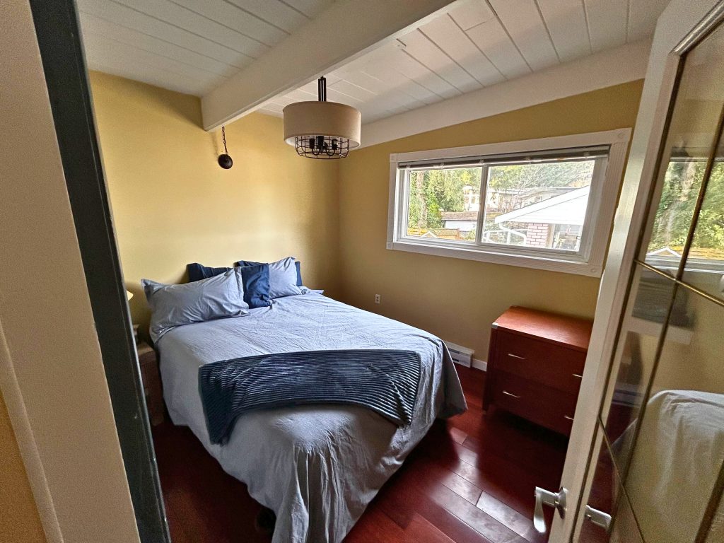 An empty room with one bed, a dresser, and a window.