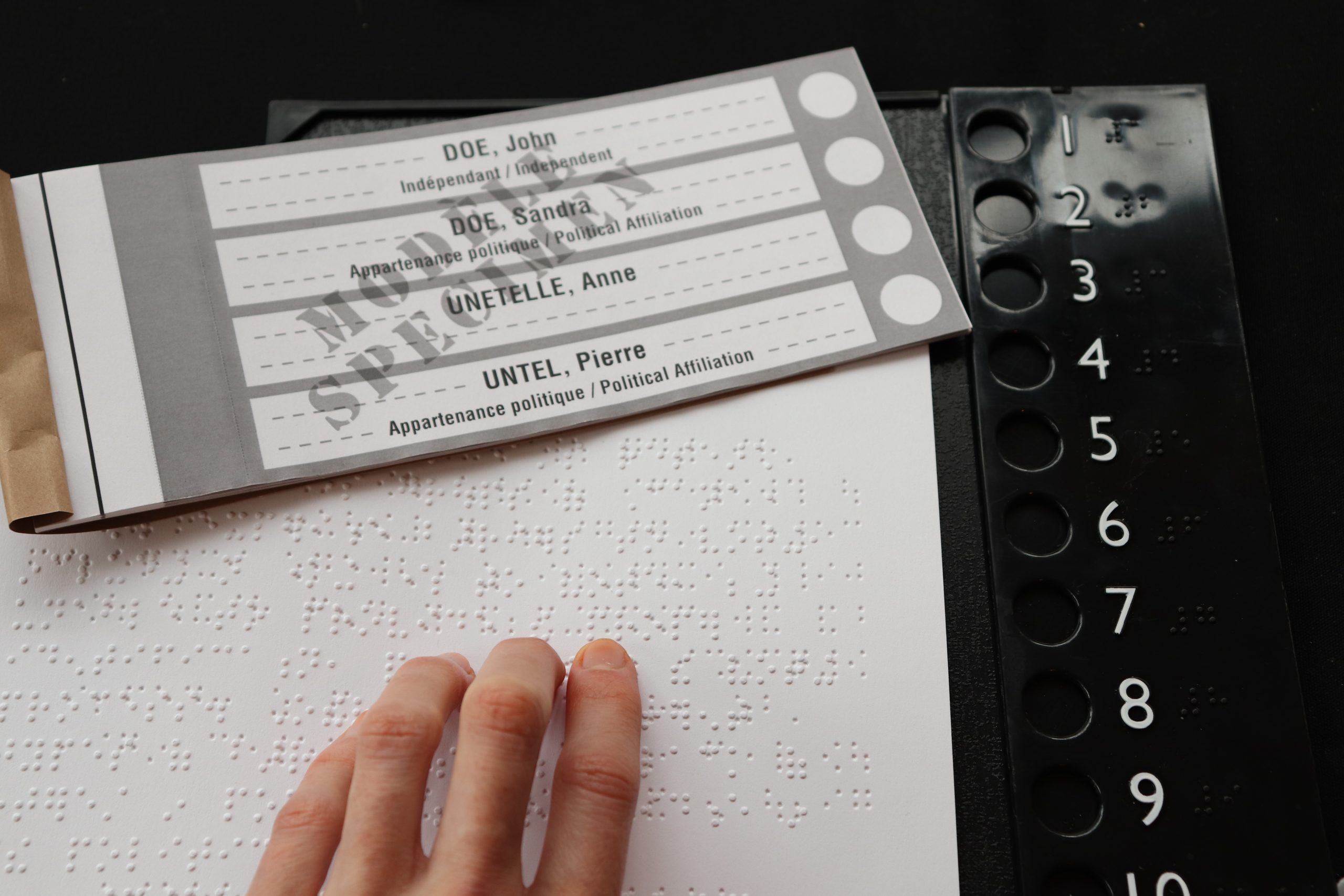 A hand on a piece of braille paper next to a blank electoral ballot.
