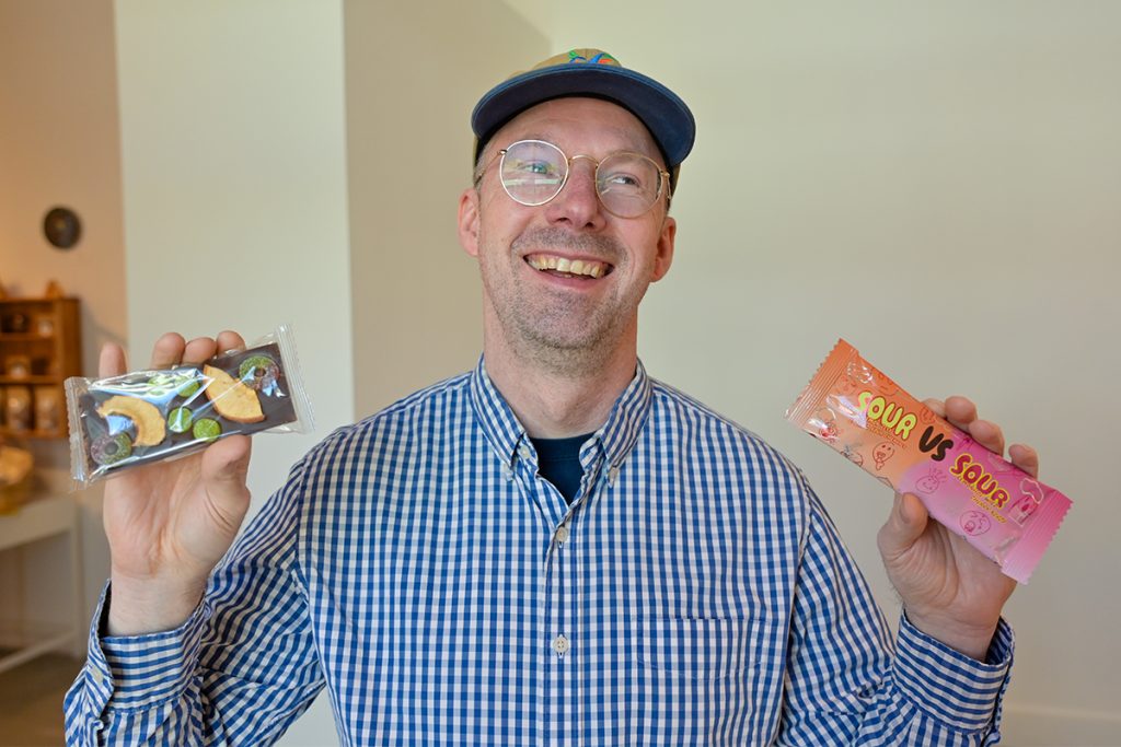 Photo of Nanaimo Art Gallery curator Jesse Birch holding up two chocolate bars that are part of the After Wrappers exhibit.