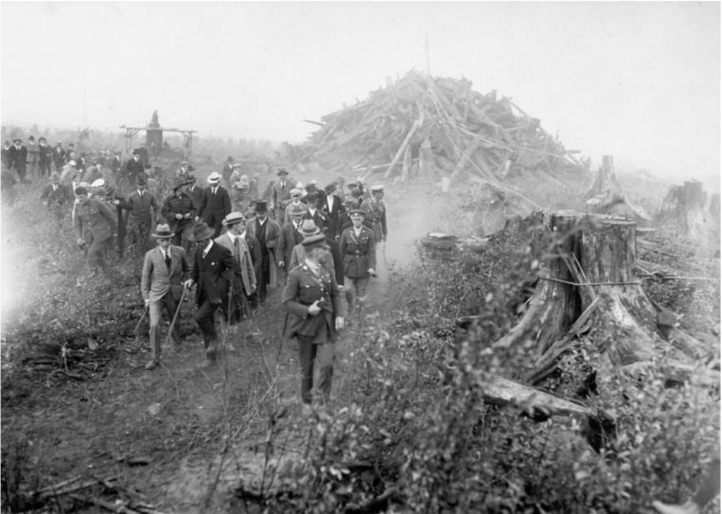 Archival image of Prince of Wales, in uniform, walking through cleared land with men following behind.