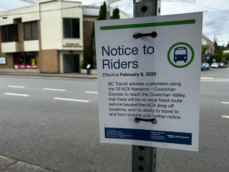 A sign with text hanging on a post in front of an empty street.