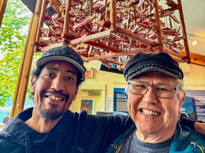 Two people are standing in front of a salmon rattle.