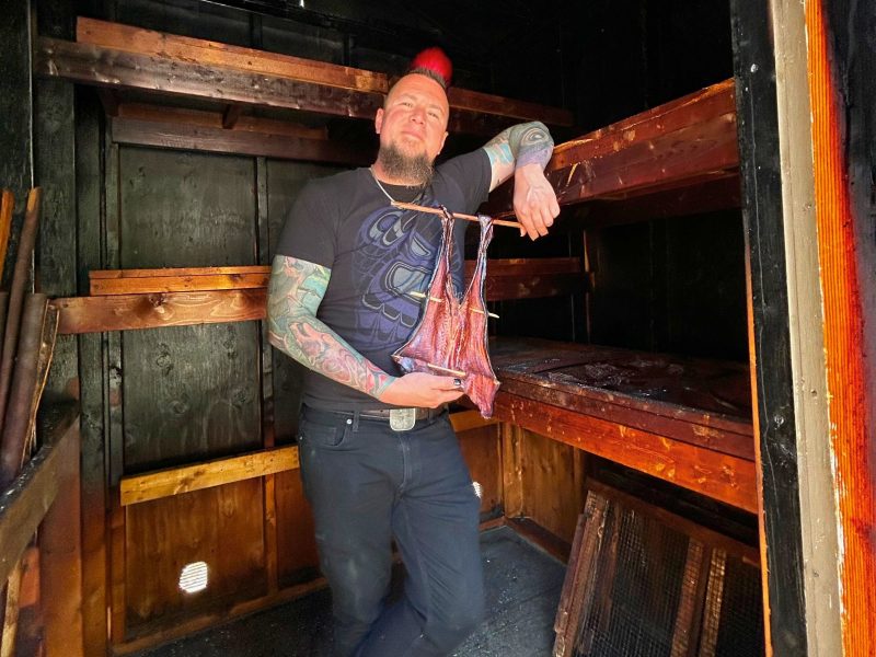 A man holding a smoked salmon in a smokehouse.
