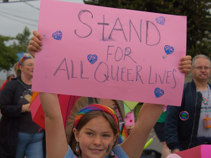 A girl holding a sign that reads "stand for all queer lives", while marching in the Cowichan Valley Pride march.