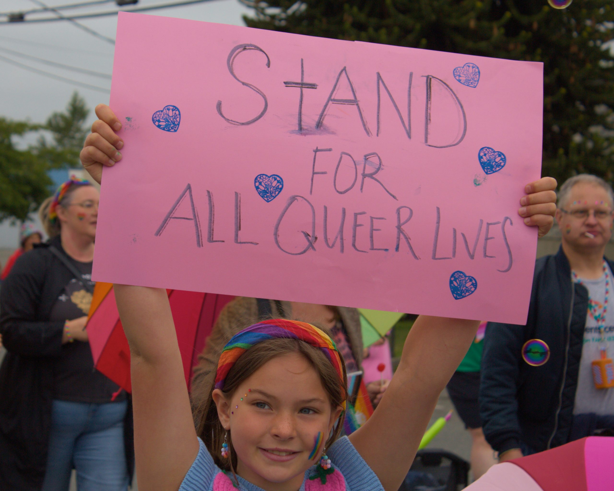 A girl holding a sign that reads "stand for all queer lives", while marching in the Cowichan Valley Pride march.