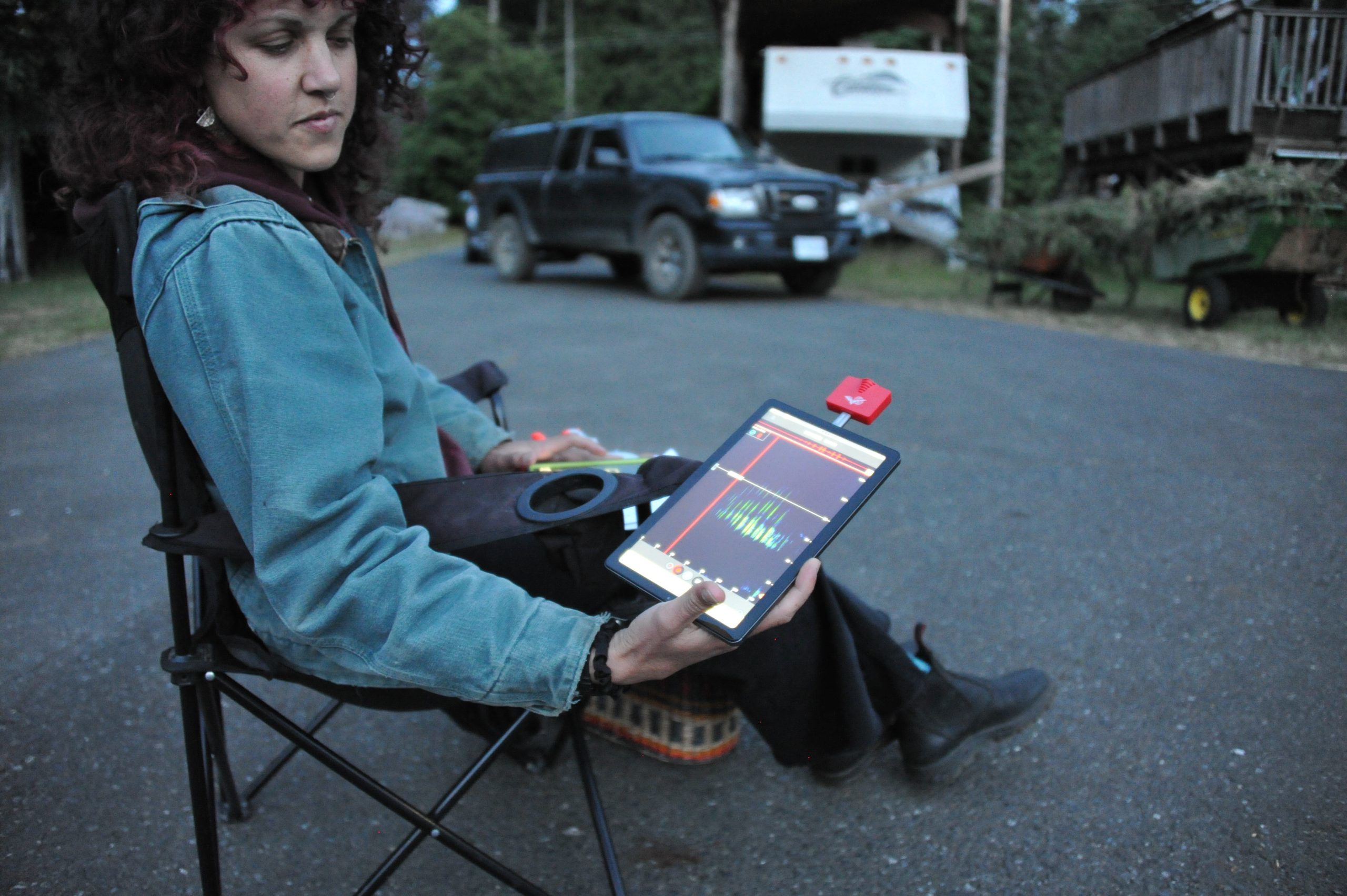A woman sits on a camp chair on the road holding a tablet with echolocation signals.