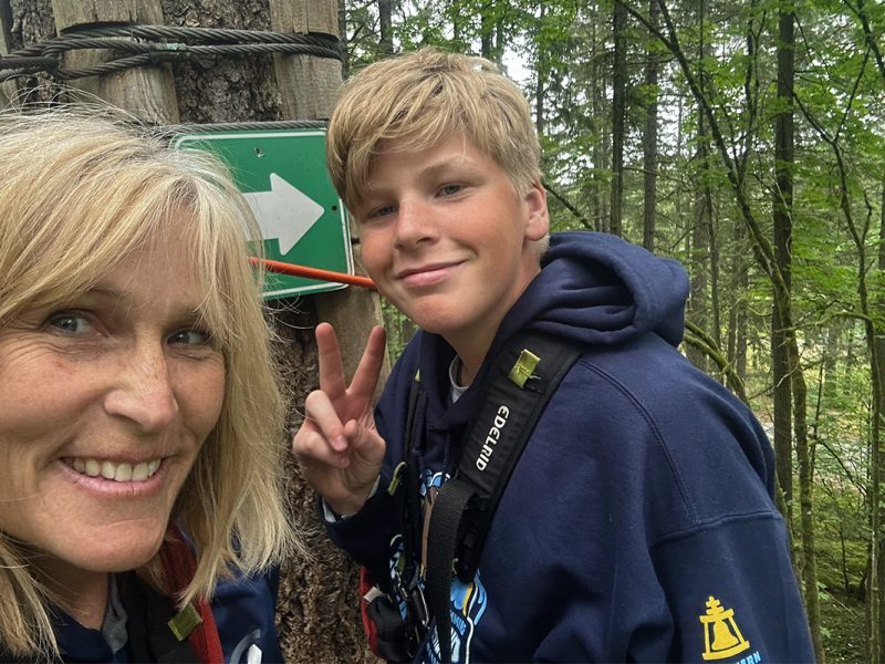 Photo of a woman and a boy outdoors in a forest with the boy giving a peace sign