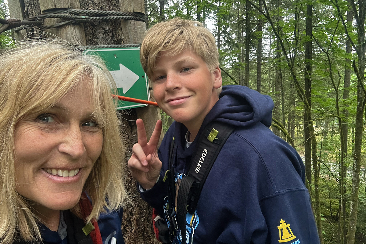 Photo of a woman and a boy outdoors in a forest with the boy giving a peace sign