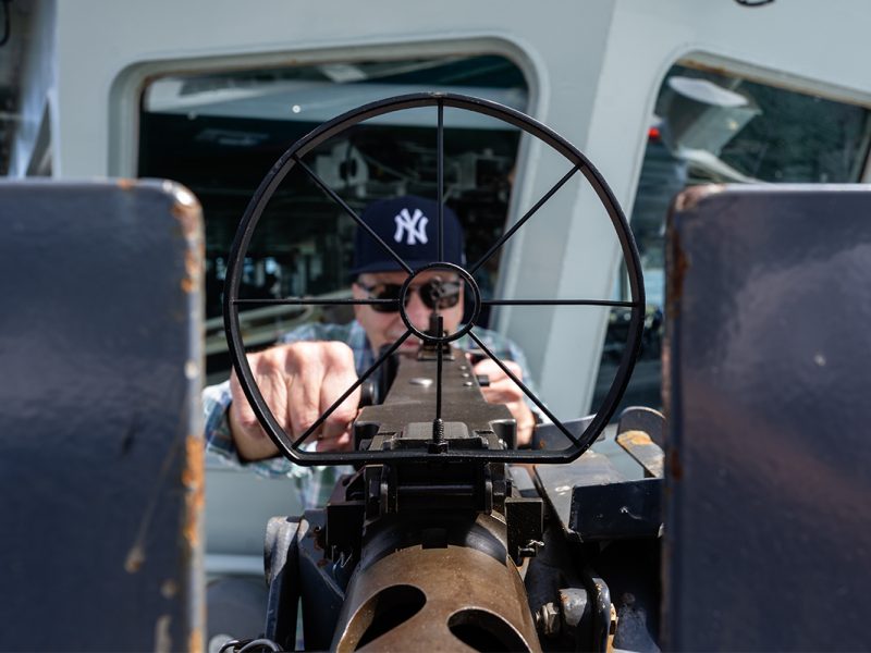 Photo of a man wearing a New York Yankees ball cap aiming down the barrel of a .50-calibre machine-gun.