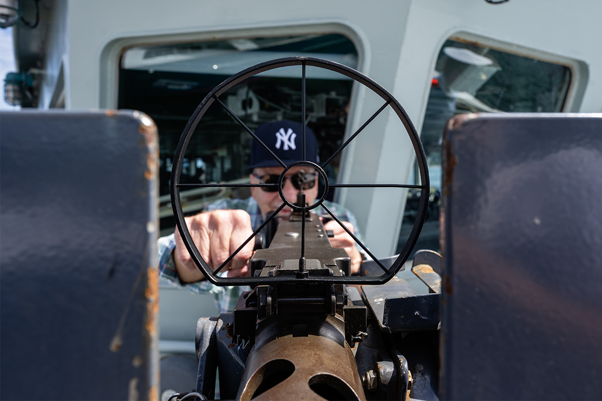 Photo of a man wearing a New York Yankees ball cap aiming down the barrel of a .50-calibre machine-gun.