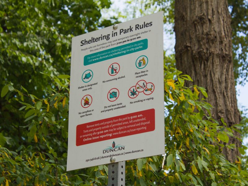 A sign on a tall metal pole that has the bylaws for overnight sheltering in the City of Duncan.
