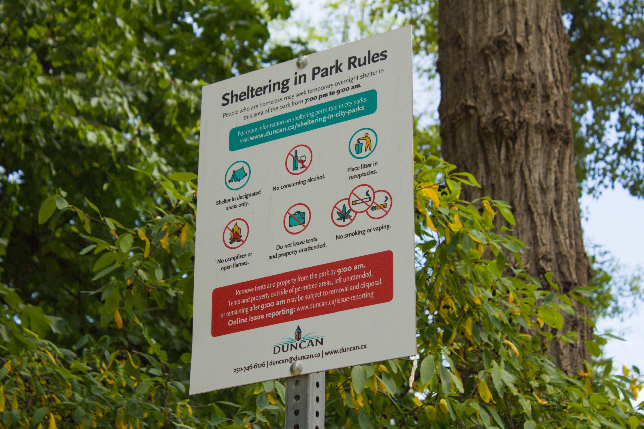A sign on a tall metal pole that has the bylaws for overnight sheltering in the City of Duncan.