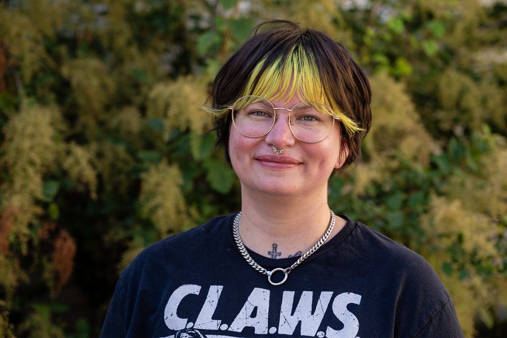 photo of bailey macabre wearing CLAWS t-shirt in front of a green bush
