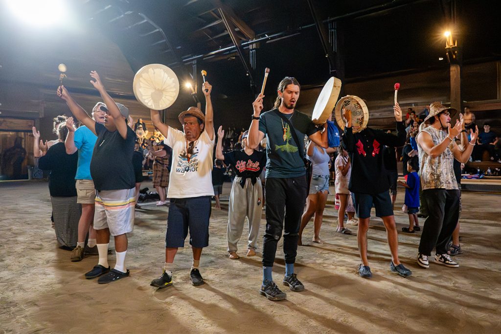 People hold up their hands and drums in thanks in the longhouse at Snuneymuxw Days 2025.