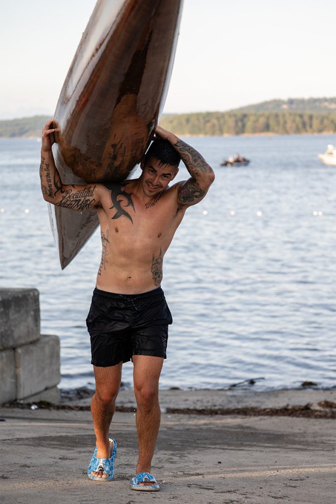 A man with tattoos carries a canoe at Snuneymuxw Days 2025.