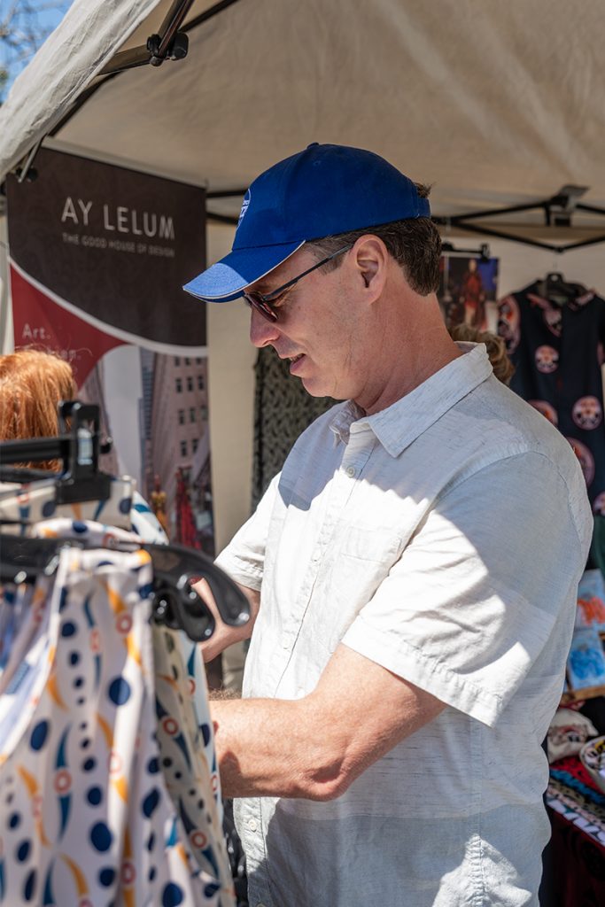 A man wearing a blue baseball cap browses a rack of clothing at Snuneymuxw Days 2025.