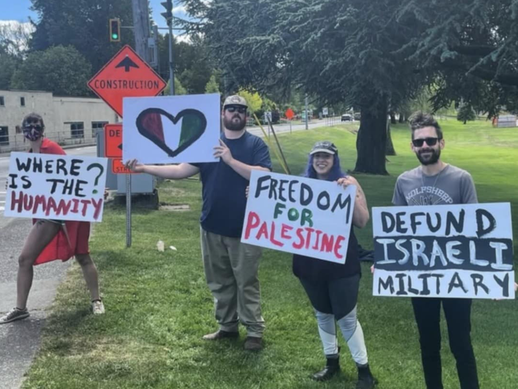 Four people stand in downtown Courtenay holding signs in support of Palestine