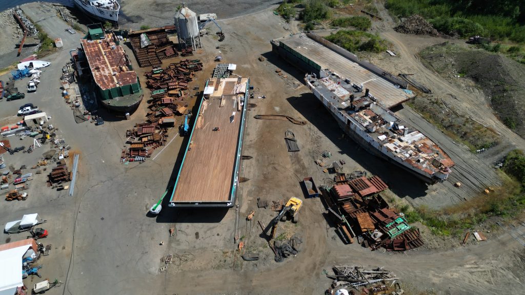Aerial view of a shipbreaking yard with three large vessels and rusty scrap metal laid out on the beach.