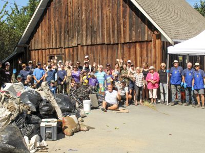 A group of people stand next to a pile of waste collected during the Cowichan River cleanup