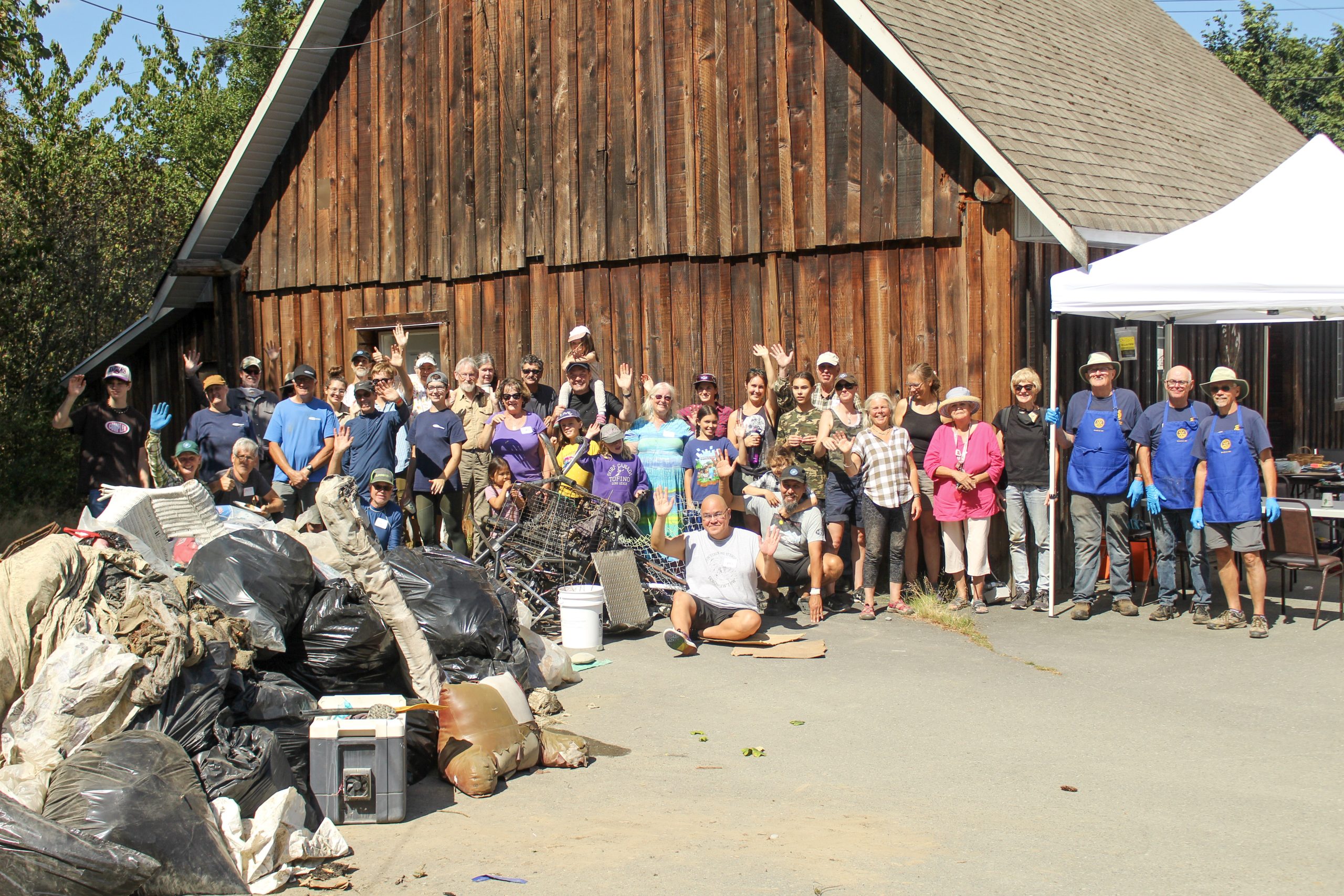 A group of people stand next to a pile of waste collected during the Cowichan River cleanup