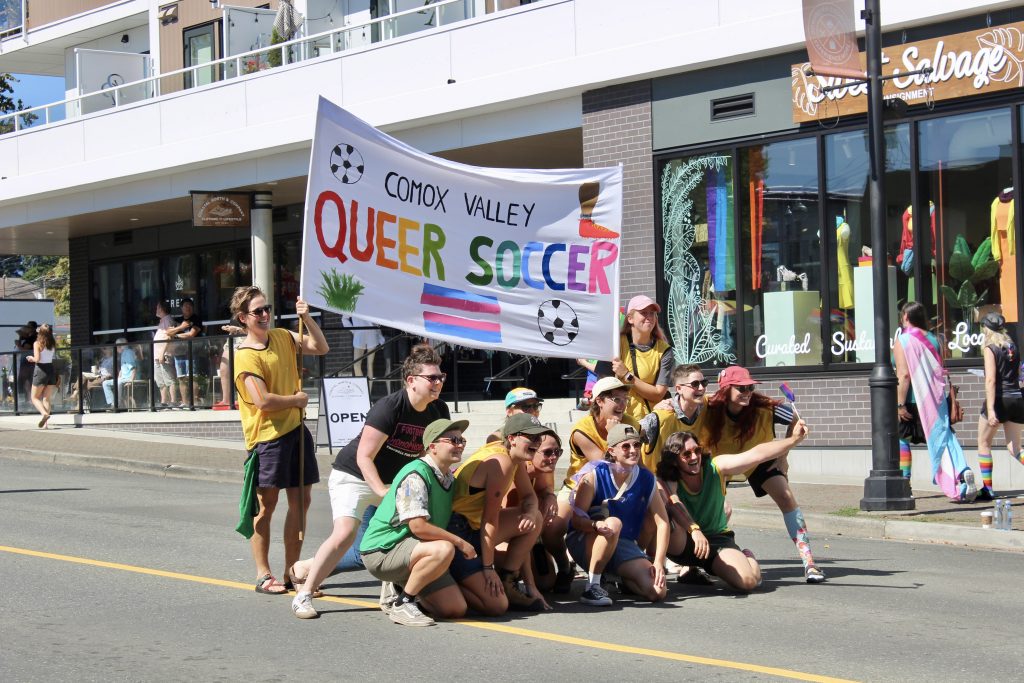 A group of people huddle together for a photo holding a banner that says 'Queer soccer'