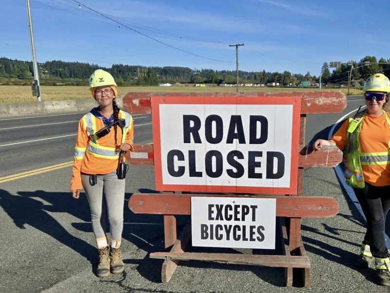 Construction workers stand next to a 'Road closed' sign